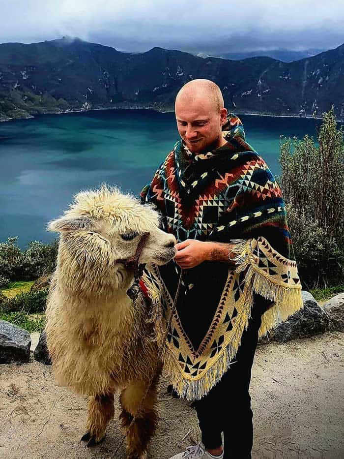 Person in poncho with llama near mountain lake